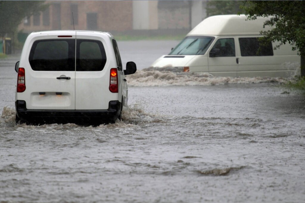 Dva biele dodávky pohybujúce sa po zaplavenej ceste.