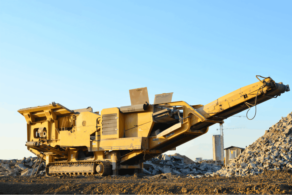 Čelusťový drvič pracujúci na stavenisku, s veľkou hromadou kameniva v pozadí.