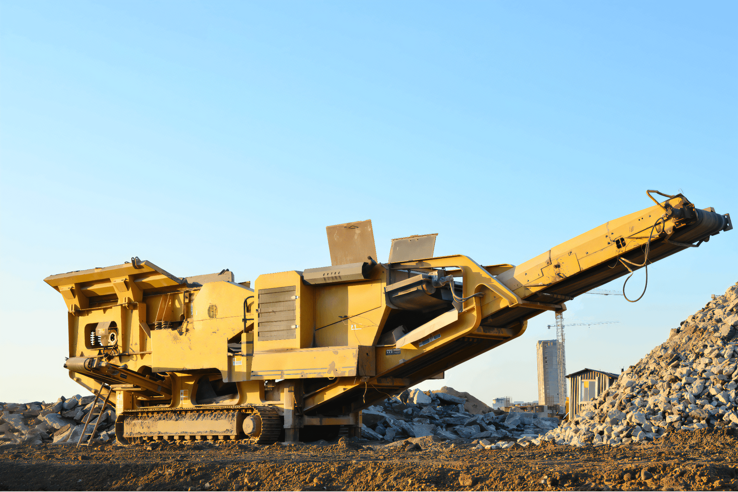 Čelusťový drvič pracujúci na stavenisku, s veľkou hromadou kameniva v pozadí.