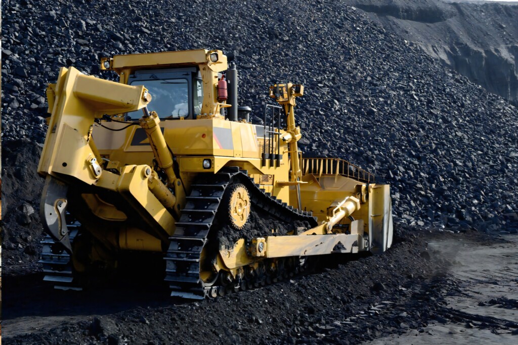 Žltý pásový buldozér pracujúci na veľkej halde uhlia.