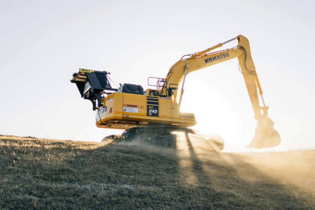 Bager Komatsu PC240 LC pracujúci na kopci pri východe slnka.