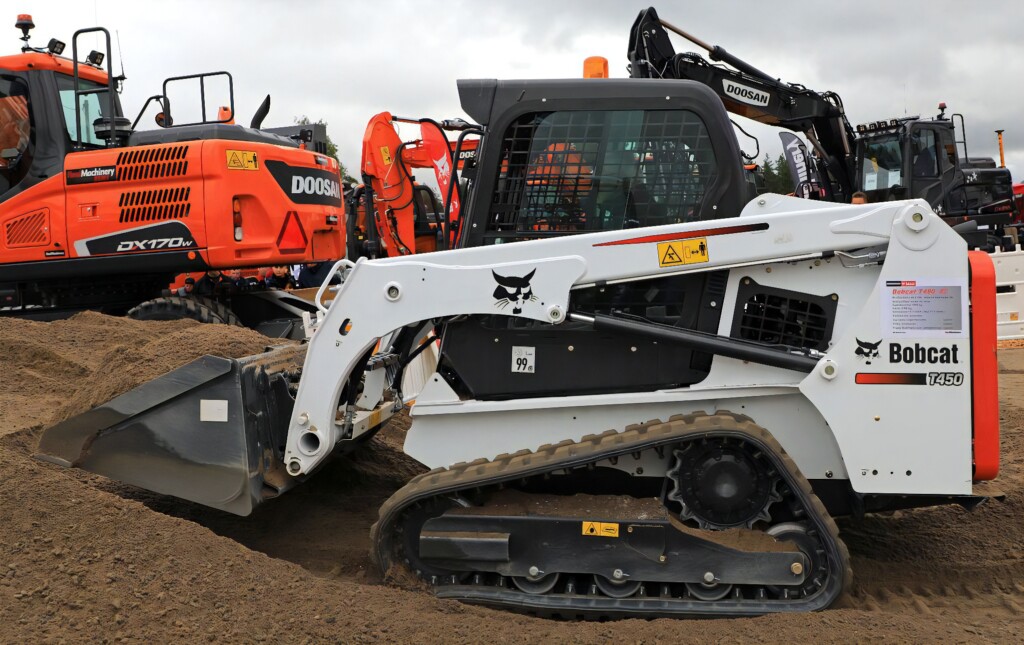 Kompaktný pásový nakladač Bobcat T450 pracujúci na stavenisku, v pozadí stavebné stroje značky Doosan.